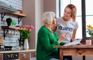 young-adult-volunteer-discussing-with-aging-woman-kitchen